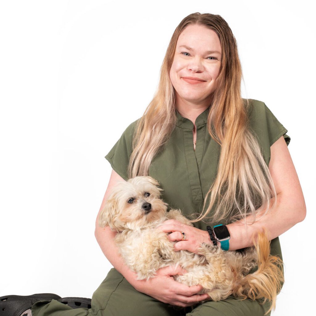 smiling veterinary technician sitting and holding a small dog